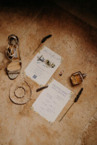flatlay du mariage avec carterie faire-part, talon Jimmy choo de la mariée, son parfum YOU de Empario Armani, les alliances et le diadèmes