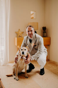le marié avec son chien le jour du mariage pendant les préparatif. avec une couronne de fleurs prévue pour la chienne. ils sont dans le salon du Mas des Costes